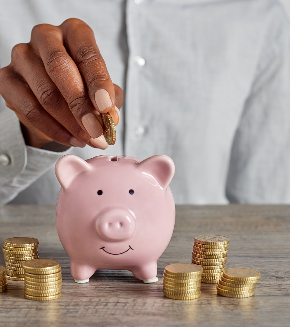 Simboliza el ahorro que consigues si compras con ésta Inmobiliaria. Hucha de cerdito con mano introduciendo moneda.